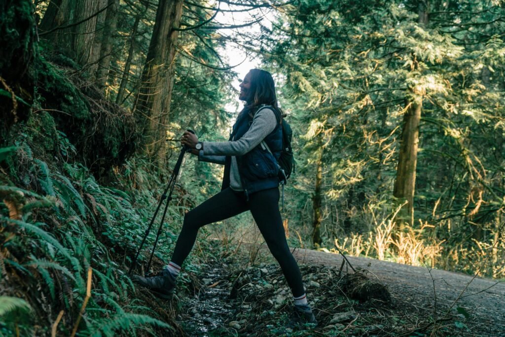 A woman hiker with trekking poles explores a green forest trail, showcasing nature and adventure.